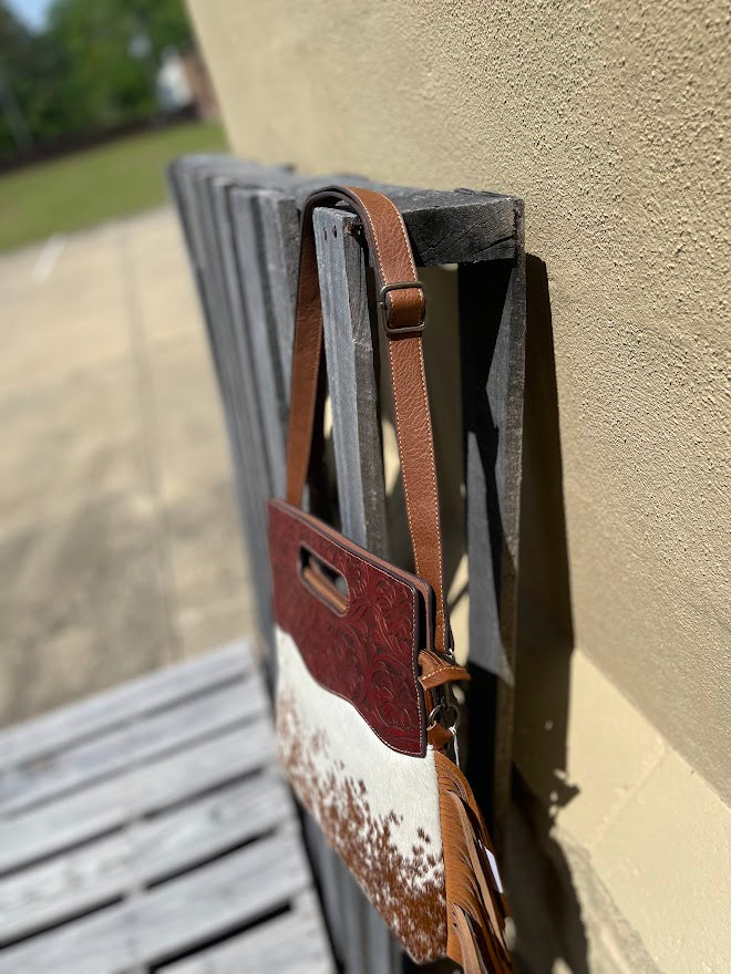 A cowhide and Brown tooled leather purse with fringe. Side view showing strap.