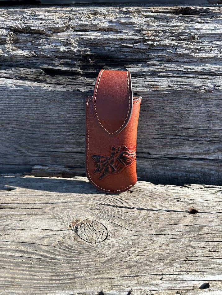 Brown leather knife sheath with a embossed Bull Rider design. It has a keep closure and a belt loop attachment. Front View