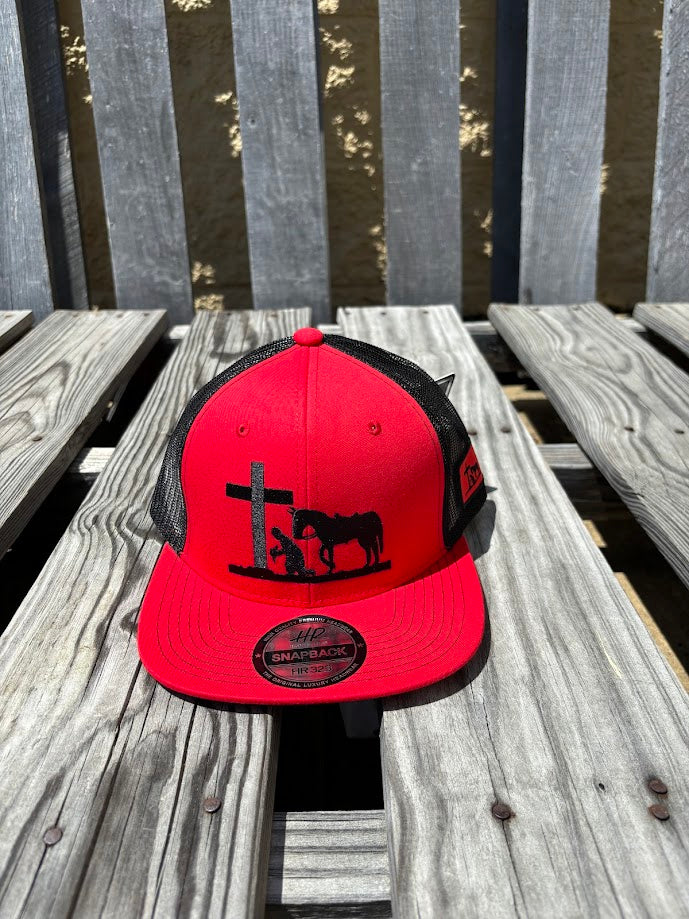 A Red and Black snapback cap with a embroidered praying cowboy design on the front. Front View