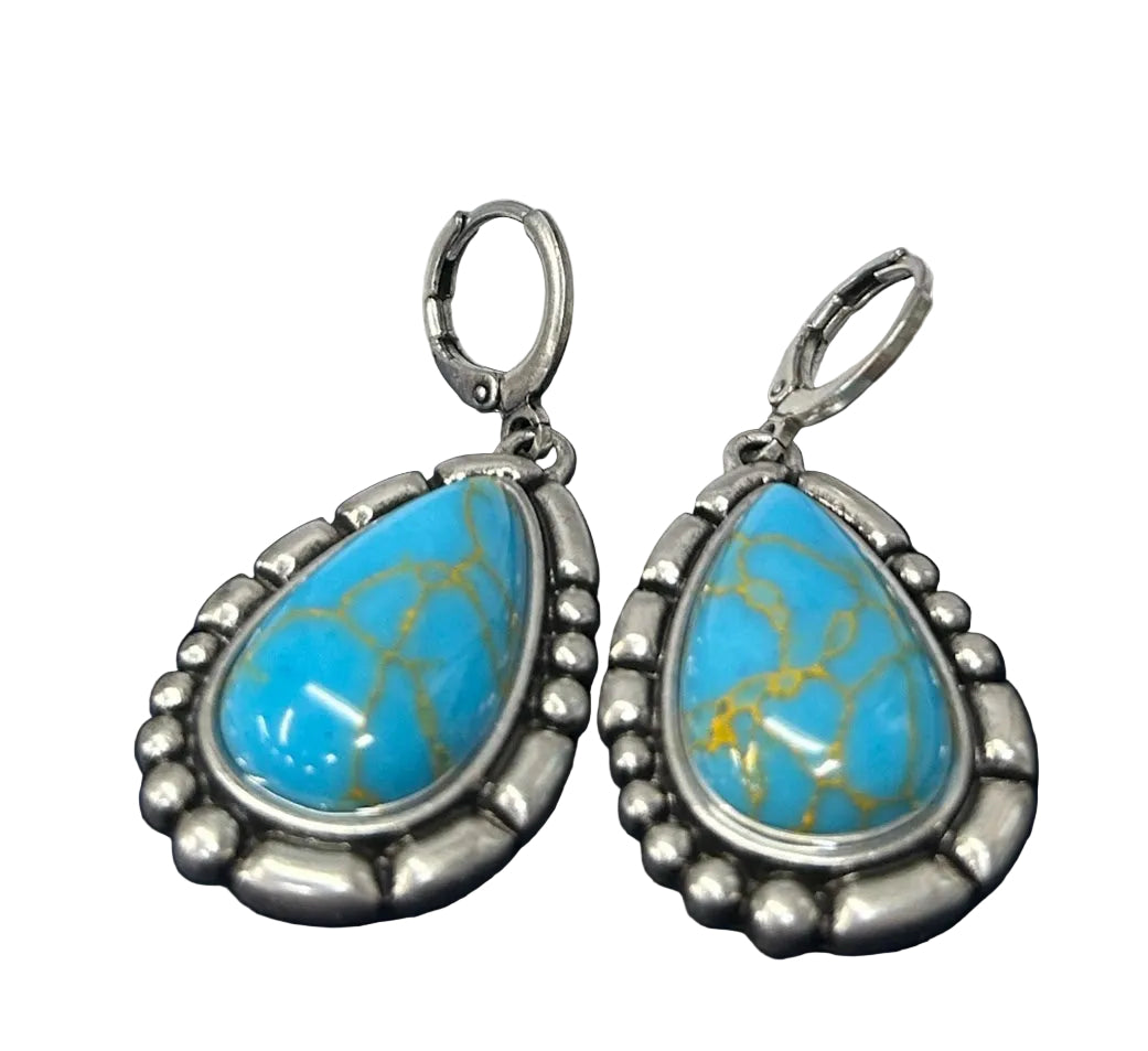 Crafted Turquoise teardrop earrings with silver border and a hinged clasp.  Close up of earrings lying down. 