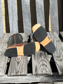 A pair of Anderson Bean 12-inch tan hungry hippo skin boots with black waxy Kansas leather tops. Bottom view featuring black hybrid outsole.