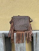 This Coffee Brown tooled leather crossbody bag has fringe sides. It has a removable and adjustable shoulder strap. It has a embossed leather front flap and a zippered closed back pocket. Front View