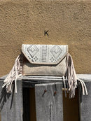 This cowhide and Beige leather bag features fringe sides and can be used as a wristlet or crossbody. It has a geometric print debossed flap with a whipstitch border.  Front View K