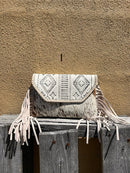 This cowhide and Beige leather bag features fringe sides and can be used as a wristlet or crossbody. It has a geometric print debossed flap with a whipstitch border.  Front View I