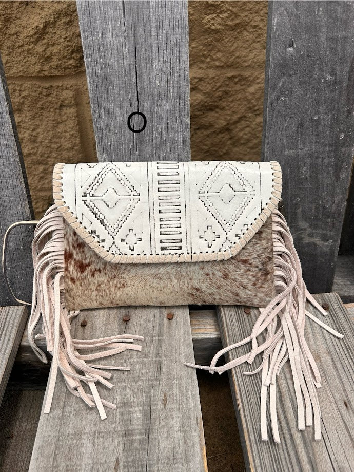 This cowhide and Beige leather bag features fringe sides and can be used as a wristlet or crossbody. It has a geometric print debossed flap with a whipstitch border.  Front View O