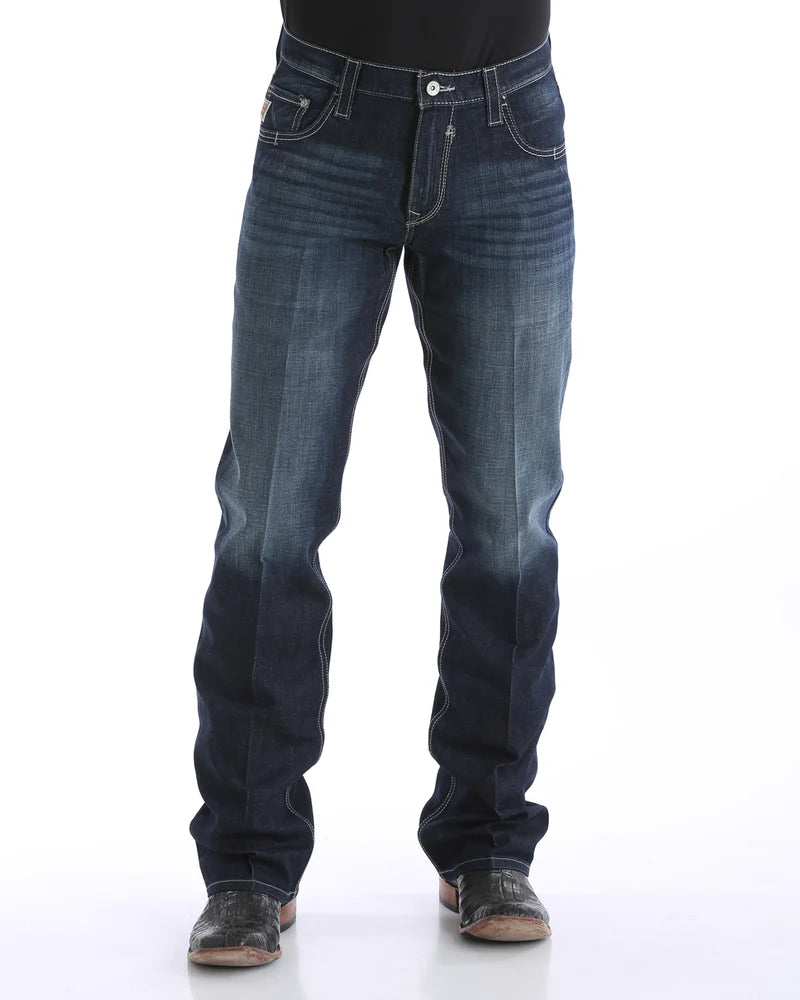 Men's Carter Dark Wash jeans front view showing whiskers, heavy sanding, and detail of front pockets and zipper. Also shows relaxed fit and boot cut stack on boots.