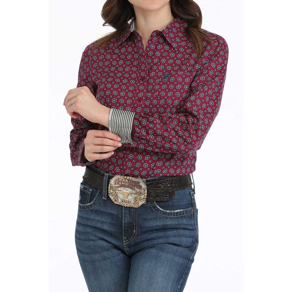 Woman wearing burgundy print Cinch long sleeve button shirt with a pair of jeans, a belt, and a western buckle. Front  view emphasizing rleft arm contrast cuff lining.