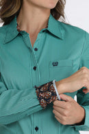 Closeup of women's Cinch long sleeve teal shirt with showing teal buttons, small left chest pocket with teal logo embroidery, and contrast fabric lining collar and cuffs. Front view.