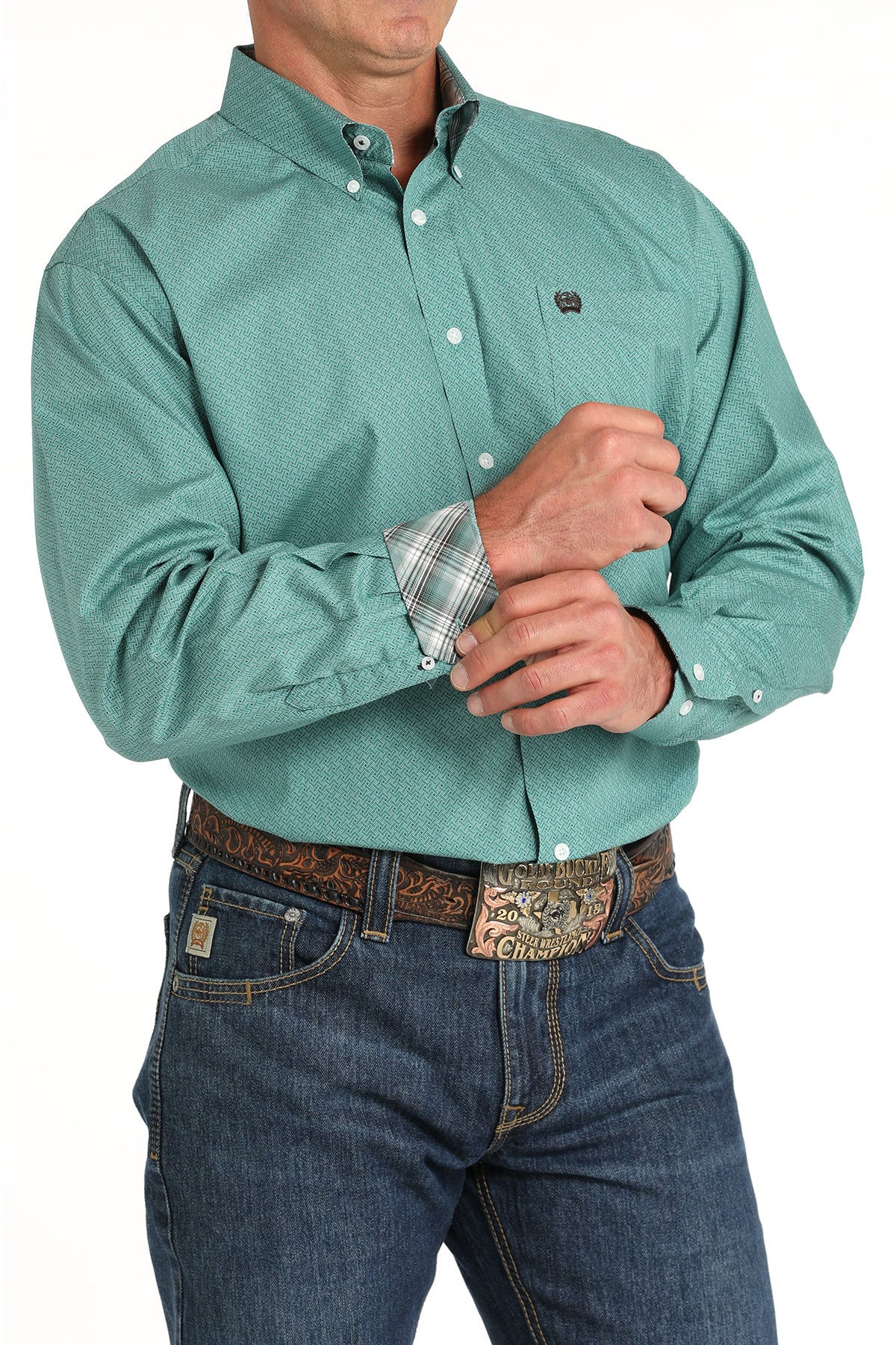 Teal print Cinch button-down long sleeve shirt  showing contrast green plaid cuff lining, 2-button adjustable cuffs, embroidered pocket logo. Also showing jeans with a belt and buckle on model. Front angled view. 