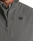  Cinch charcoal grey nylon-spandex ripstop windproof vest. Has full front zipper, slash zippered hand pockets, left chest vertical zippered phone pocket, left chest black embroidered logo, lined standing collar. Has zipper wind liner. Hits low hip. Close up view of zipper close, pocket, and Cinch logo on chest. 