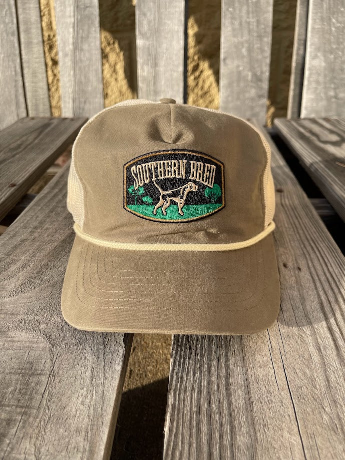 A loden green and beige 'Southern Bred Apparel Company' snapback cap with a logo on the front, placed on a wooden surface.