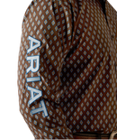 Men's Ariat long sleeve team logo shirt in brown with a blue diamond pattern. Close up of left sleeve showing bold Ariat team logo. 