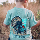 A lifestyle photo of a little boy wearing a Khaki short-sleeved children's T-shirt with a graphic print of a turkey and the brand name 'Fieldstone'.