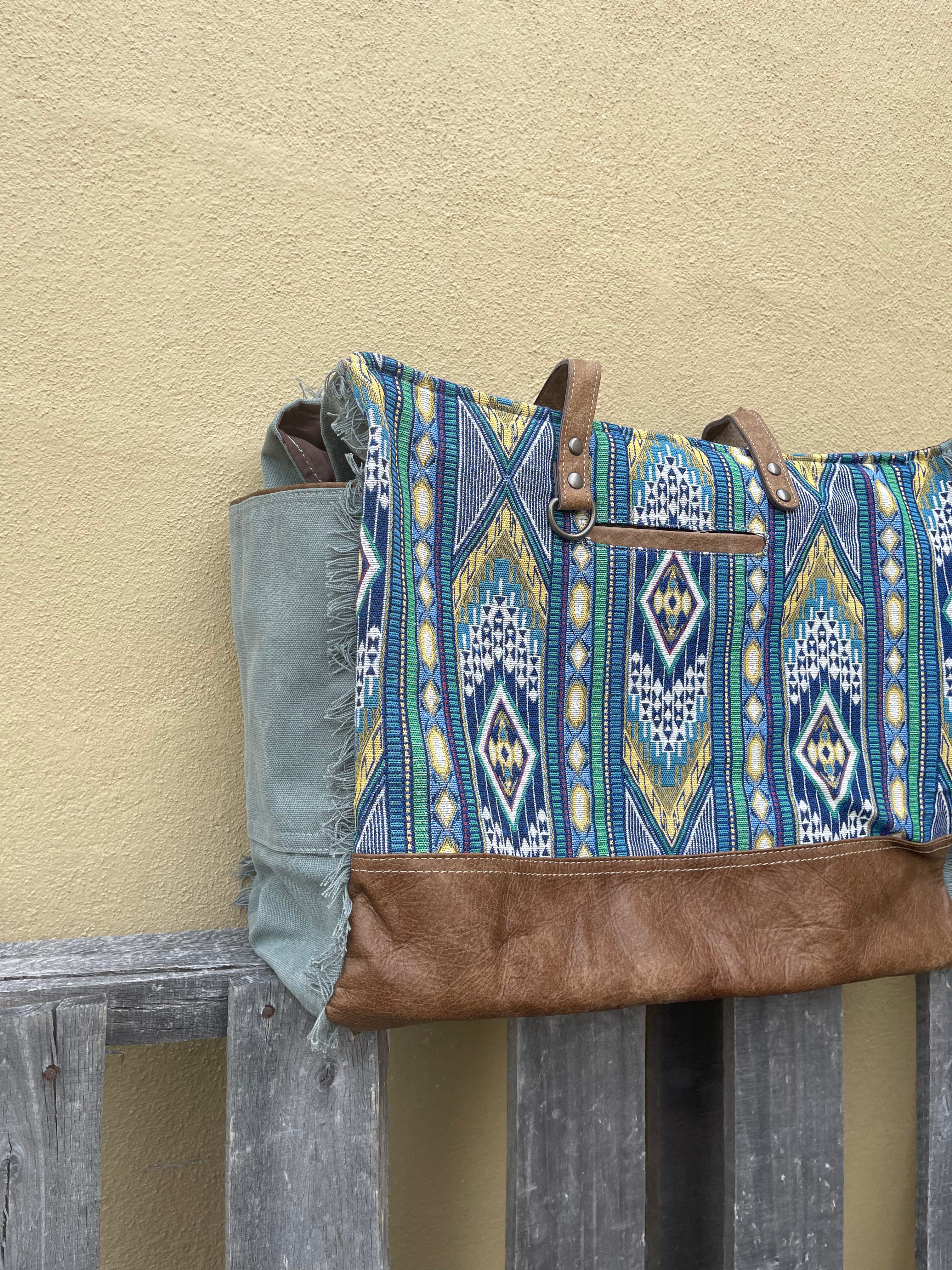 A blue multi canvas and leather conceal carry weekender bag with a geometric pattern. Side view showing pockets. 