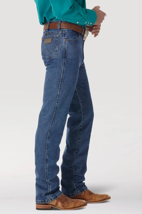 Side view of a man wearing Wrangler® Cowboy Cut® Slim Fit Stonewashed Jean with a western shirt, belt, and boots. This view shows the right front scoop pocket with the top corner rivets, a right coin pocket, and the right back pocket with the ".W" top stitched below a neolite logo patch.