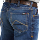 Men's Ariat FR boot cut jean in a M4 relaxed fit, this jean is a medium wash. Close up of back pocket details showing stitching and Ariat FR logo tag. 