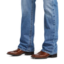 Men's Ariat M4 relaxed fit boot cut jean in a light wash.  Bottom view showing leg opening over jeans. 