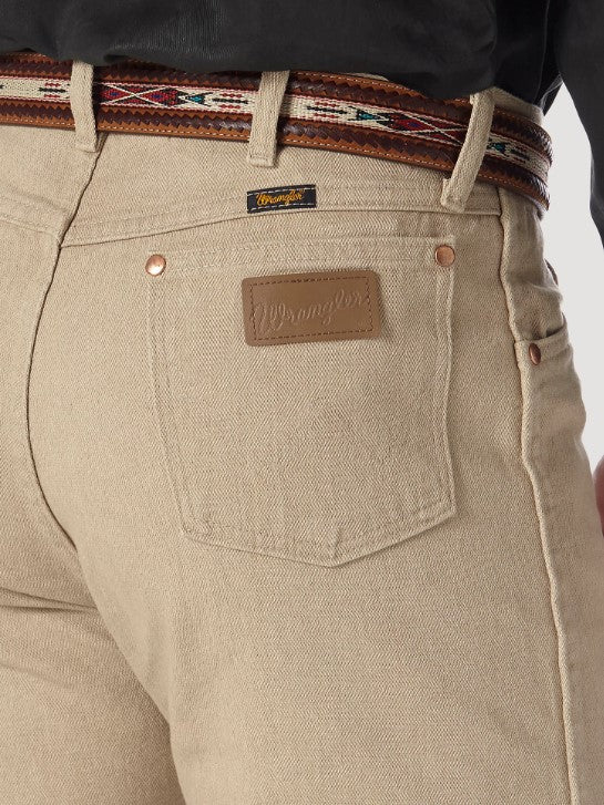 Closeup of back right back pocket of a man wearing Wrangler® Cowboy Cut® tan prewashed original fit jeans with western shirt and belt. Pocket has copper rivets on top corners  and neolite brown logo patch.