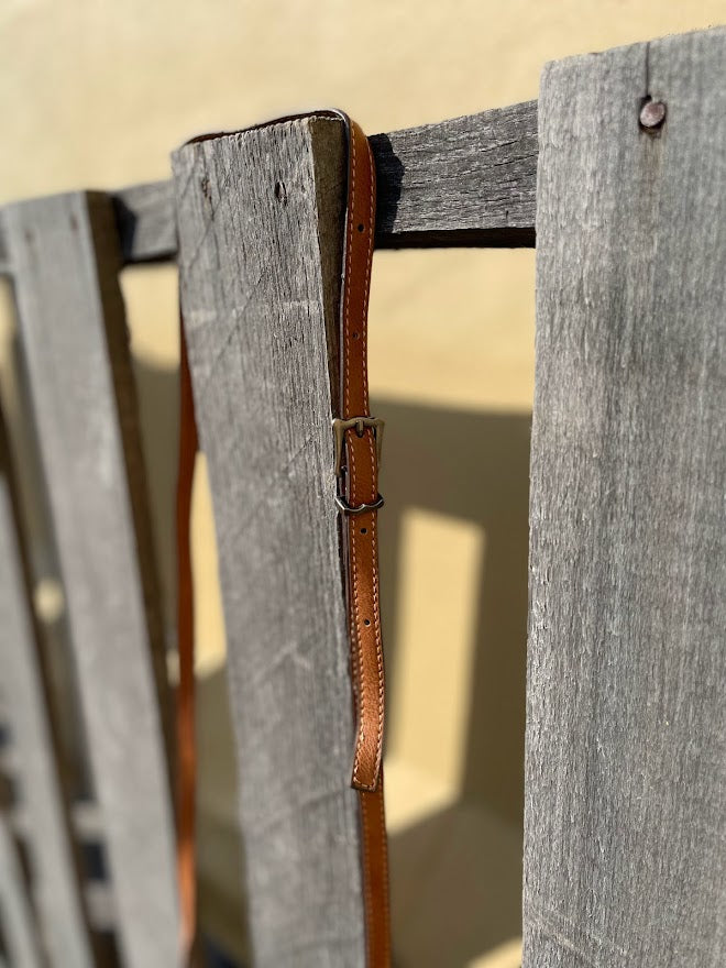 This Brown tooled leather and cowhide bag features side fringe. Close up view of adjustable shoulder strap. 
