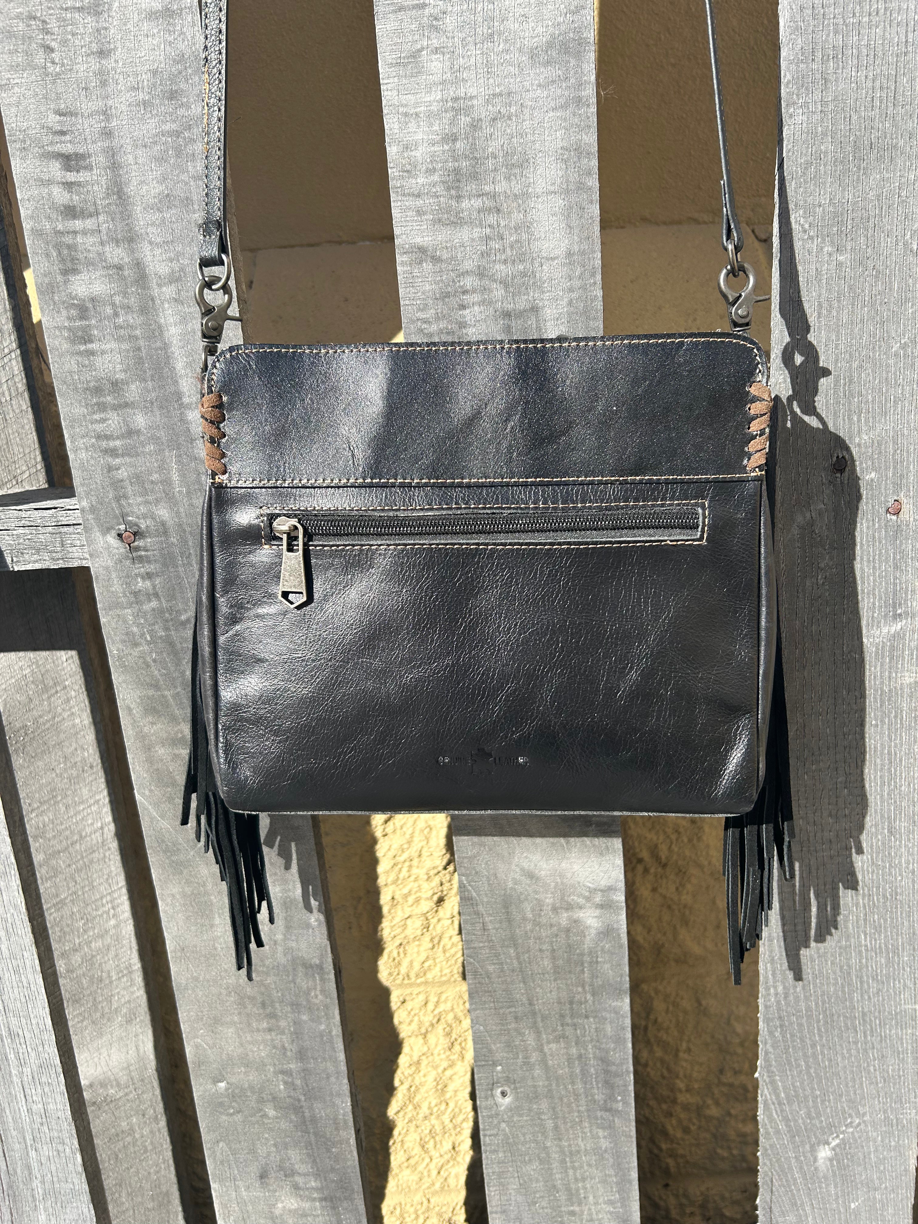 Black embossed leather and cowhide crossbody bag with side fringe. This bag features a zippered closed top and a removable, adjustable strap. Rear View