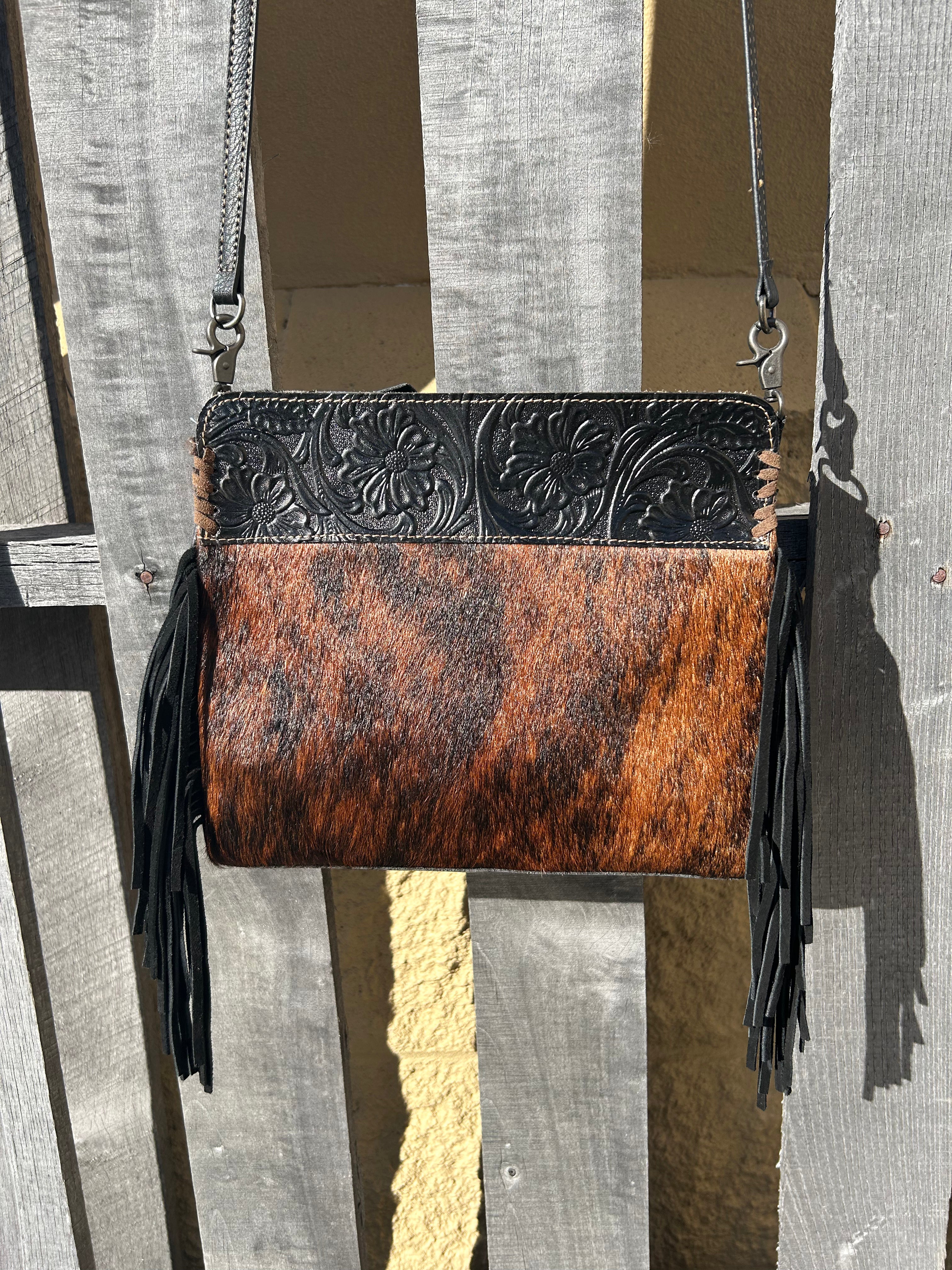 Black embossed leather and cowhide crossbody bag with side fringe. This bag features a zippered closed top and a removable, adjustable strap. Front View A