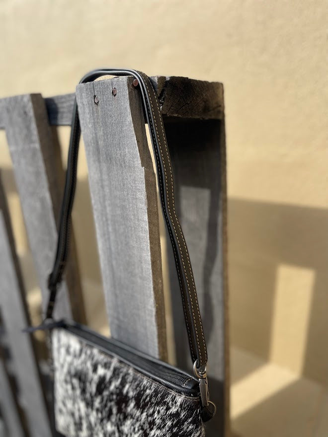Black leather and cowhide wristlet bag that also comes with a removable adjustable crossbody strap. This is a larger wristlet with a inside zip close pocket and credit card slots. Side view showing shoulder strap. 
