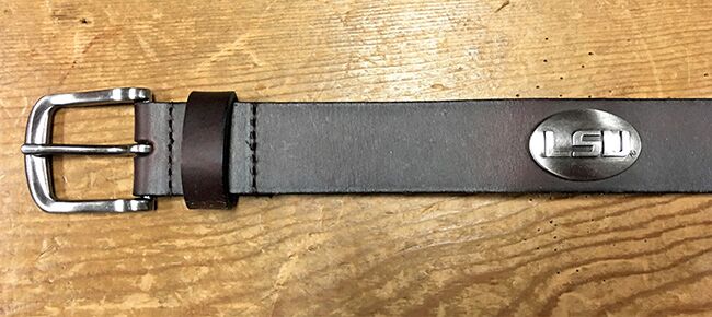 A Zep-Pro brown leather belt laid flat to show a silver metal buckle and an oval LSU silver tone concho. 