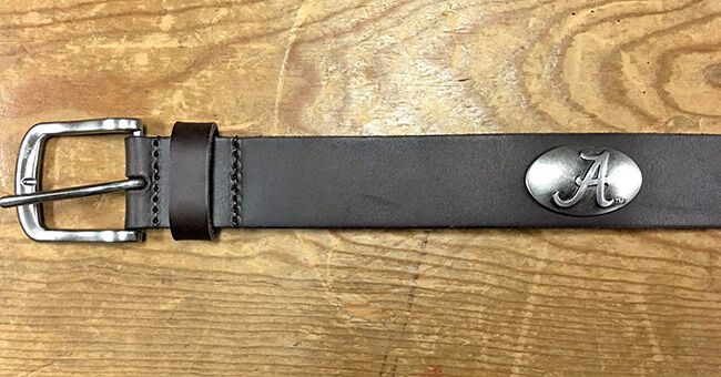 A Zep-Pro brown leather belt laid flat to show a silver metal buckle and an oval Alabama logo "A" silver tone concho. 