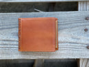 A light brown bifold leather wallet with a beige inlay design and a praying cowboy design. Rear view showing additional card slot. 