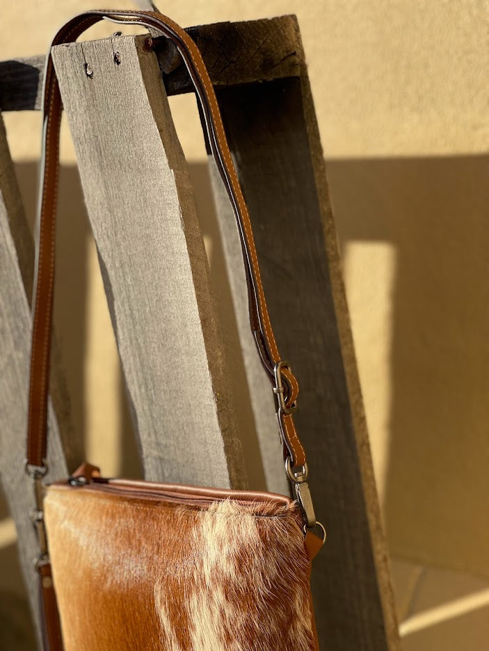 Cowhide wristlet with detachable crossbody strap with a solid Brown leather back. Side view showing shoulder strap. 