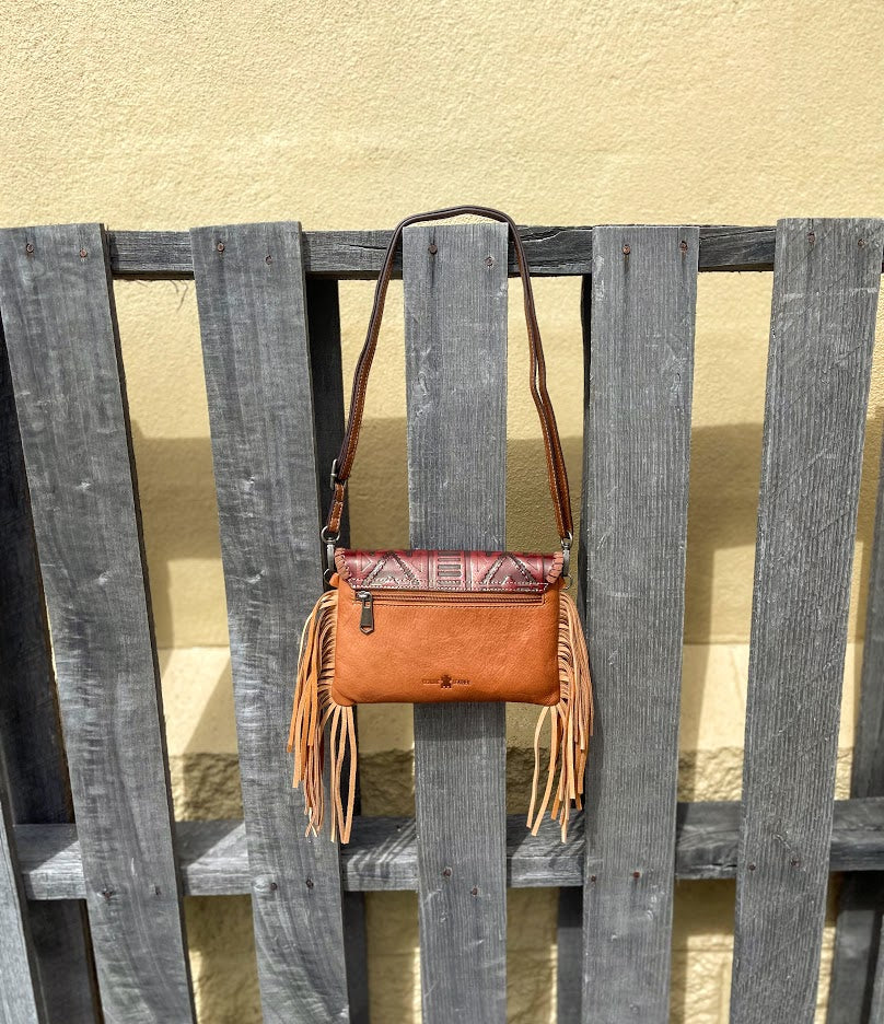 Cowhide purse with Brown leather embossed flap and tassel detail. Has a removable, adjustable shoulder strap and a wristlet strap. Rear view showing zippered close pocket. 