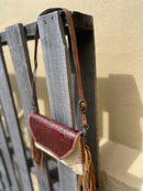 Cowhide purse with Brown leather embossed flap and tassel detail. Has a removable, adjustable shoulder strap and a wristlet strap. Side view showing shoulder strap. 