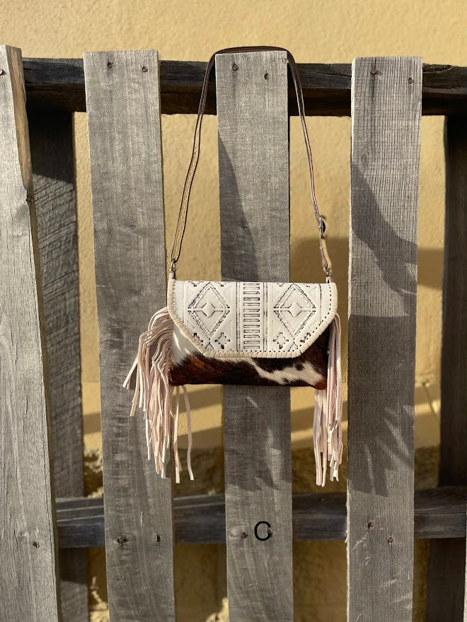 This cowhide and Beige leather bag features fringe sides and can be used as a wristlet or crossbody. It has a geometric print debossed flap with a whipstitch border.  Front View C