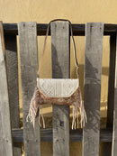 This cowhide and Beige leather bag features fringe sides and can be used as a wristlet or crossbody. It has a geometric print debossed flap with a whipstitch border.  Front View E