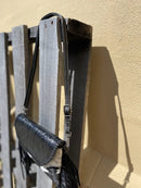 This cowhide and black leather crossbody bag has fringe sides. It features a whipstitch flap closure with a geometric design. Side view showing shoulder strap.