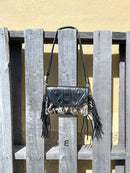 This cowhide and black leather crossbody bag has fringe sides. It features a whipstitch flap closure with a geometric design. Front View E