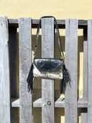 This cowhide and black leather crossbody bag has fringe sides. It features a whipstitch flap closure with a geometric design. Front View G