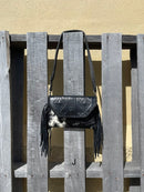 This cowhide and black leather crossbody bag has fringe sides. It features a whipstitch flap closure with a geometric design. Front View J