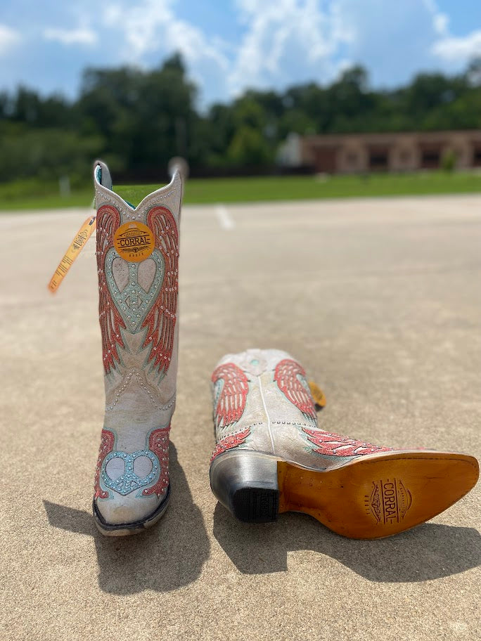 A pair of Women's Corral 13-inch heart and wings snip toe boots with studded cowhide inlay. Front View with one boot laying down to show leather outsole, leather heel with its rubber bottom.