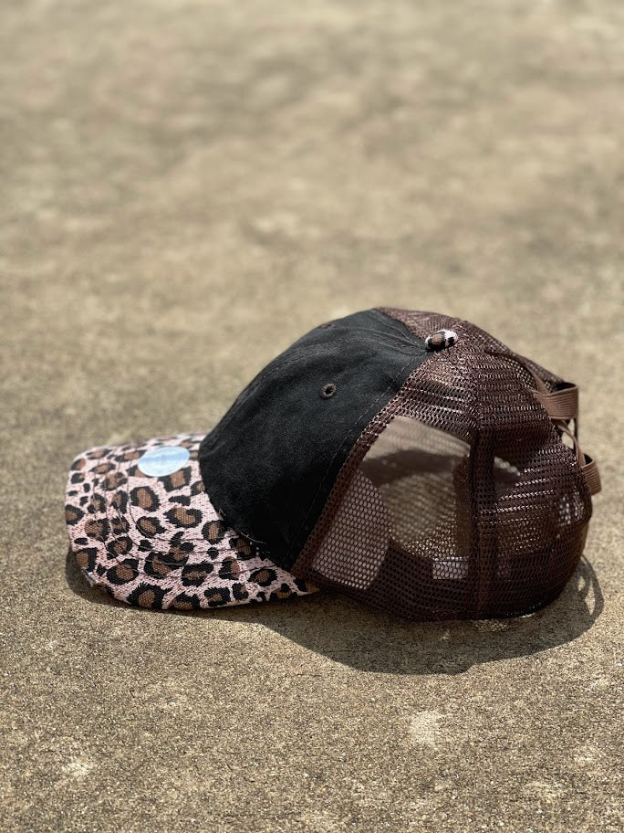 This cap has a distressed black front, brown mesh back and a brown leopard bill. The back has elastic crisscrossing bands and a adjustable Velcro back for a truly adjustable fit for your ponytails or buns. Side View 