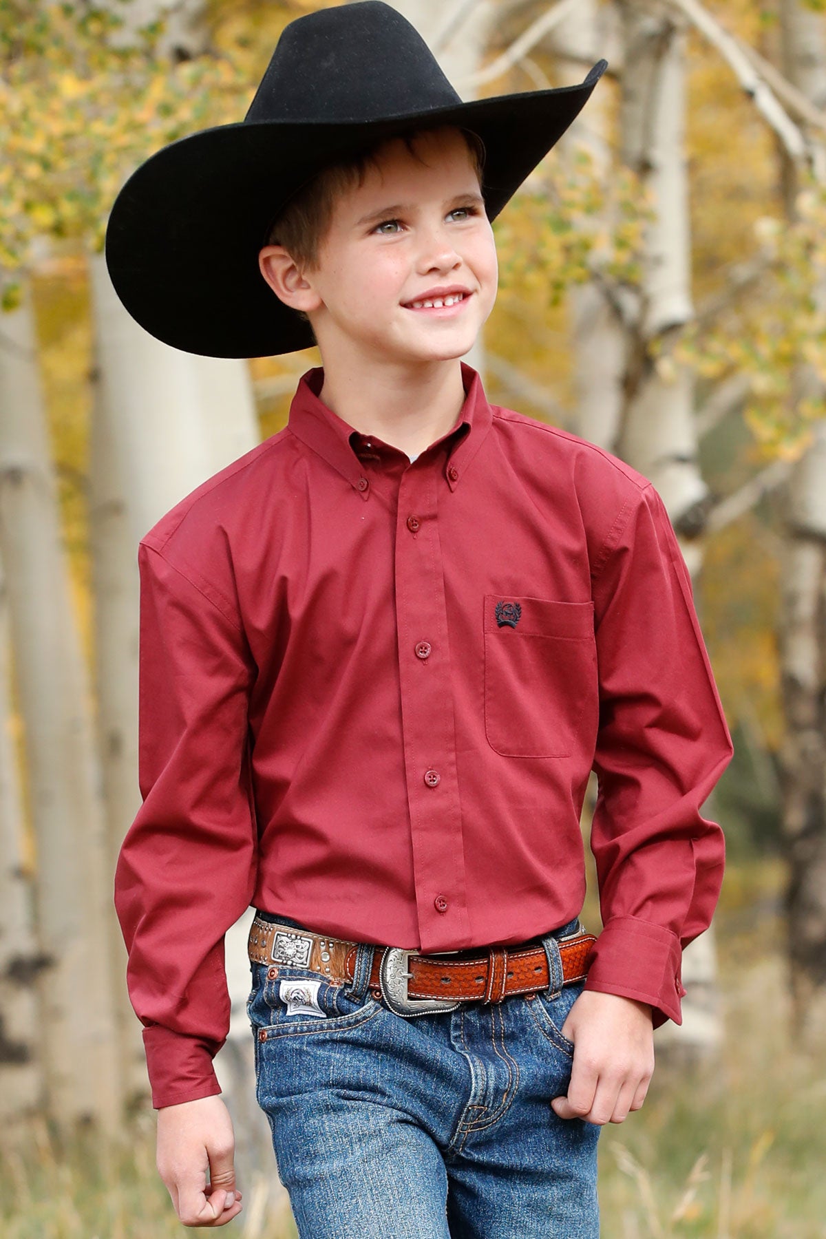 A boy wearing a red long sleeve button down shirt with an embroidered logo on the pocket.