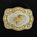 A silver and gold tone belt buckle with a motif of a bull rider, floral scroll edges, and stars in the corners.