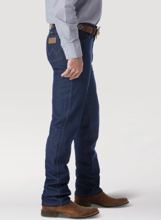 A man wearing Wrangler® Cowboy Cut® slim fit rigid blue jeans with western shirt, belt, and boots. Side view shows brown neolite patch on right back pocket.