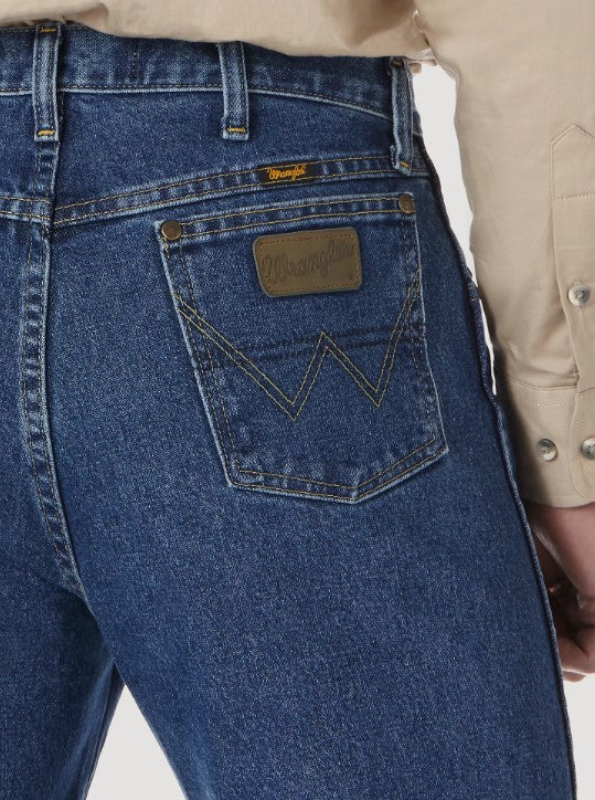 A close-up view of the back pocket of a Wrangler men's George Strait Cowboy Cut original fit jeans showing the top rivets, faux leather logo patch, and the "W" stitching.