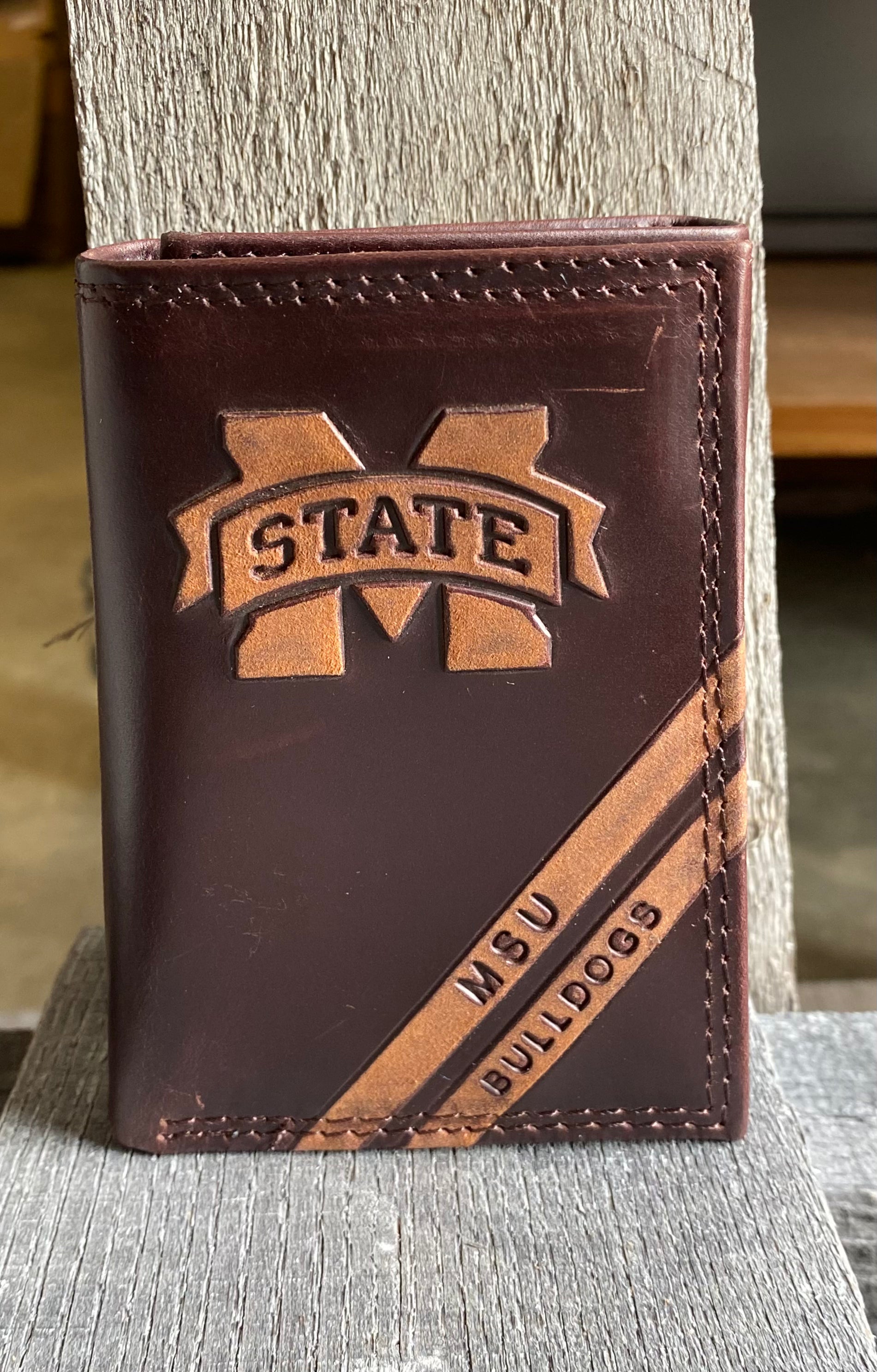A Zep-Pro brown leather trifold wallet featuring the Mississippi State University MSU logo in debossed design. Two debossed stripes angled on the bottom right read MSU Bulldogs. Front view. 