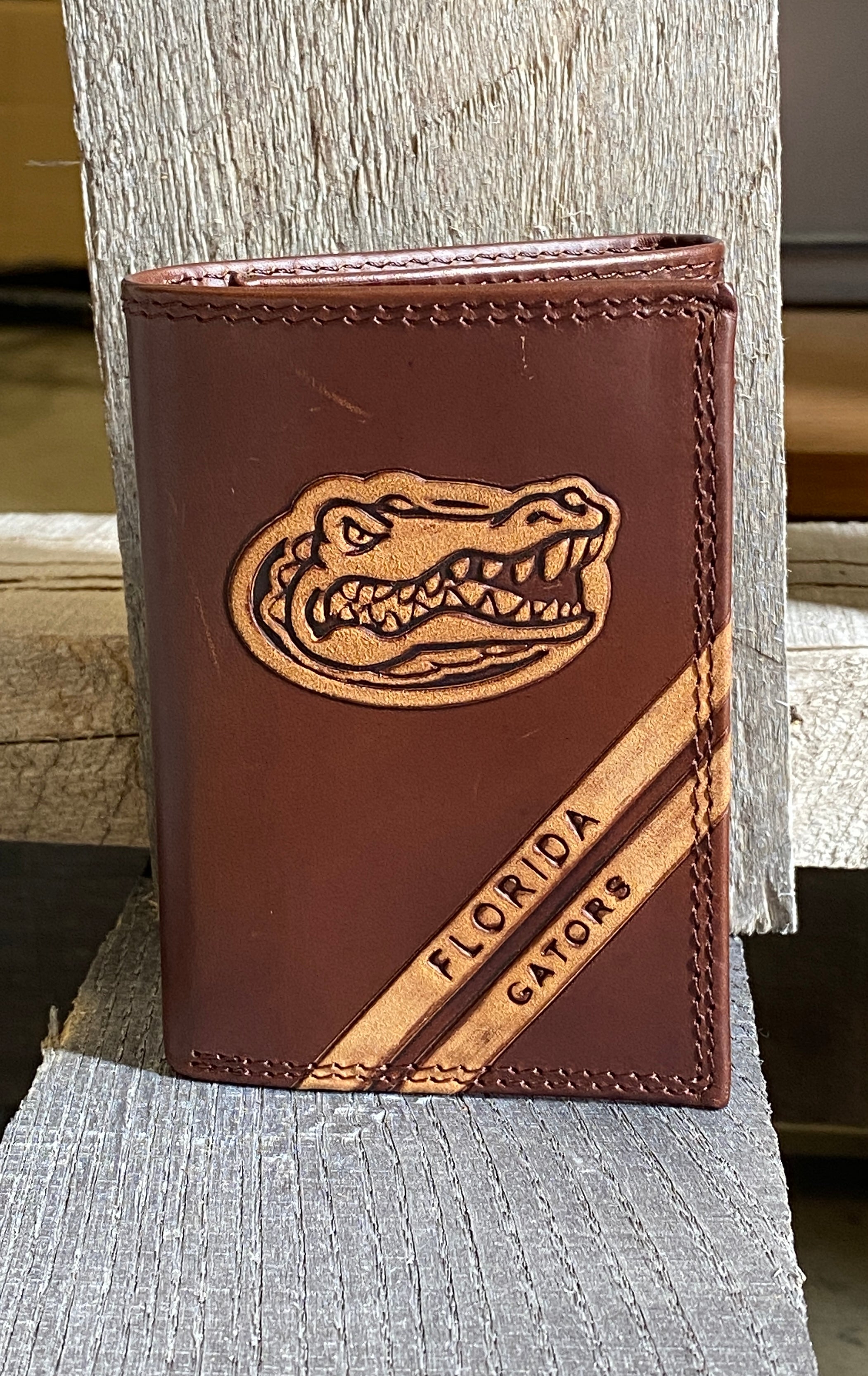  A Zep-Pro brown leather trifold wallet featuring the  University of Florida Gators logo near the wallet top in debossed design. Two debossed stripes angled on the bottom right read Florida Gators. Front view.