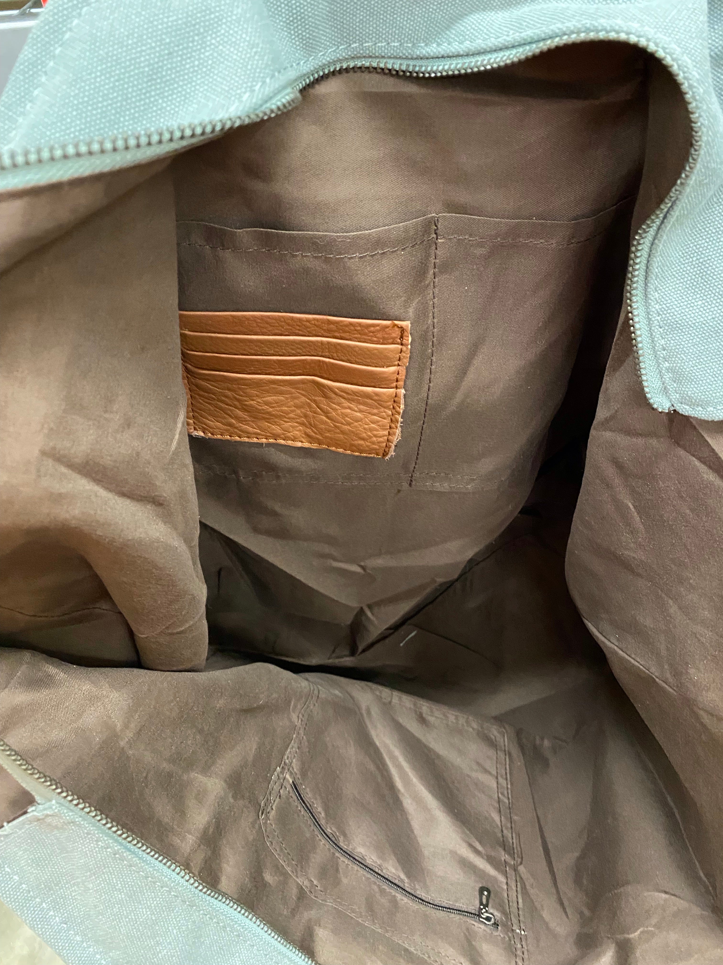 A blue multi canvas and leather conceal carry weekender bag with a geometric pattern. Inside view showing three credit card slots, a zippered closed pocket, and two additional pockets. 