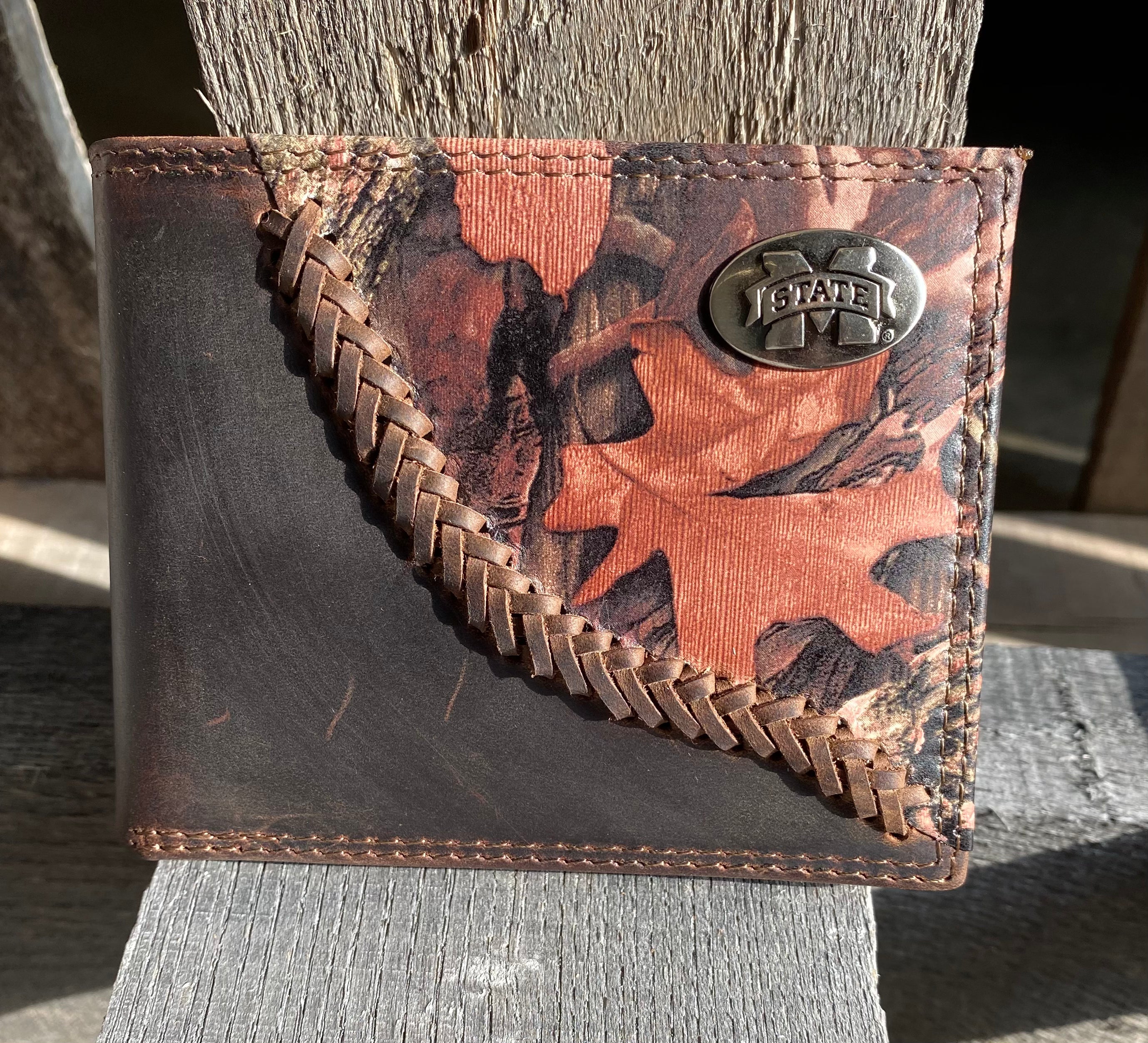 Zep-Pro Mississippi State University 1/2 Mossy Oak Camo/Brown Leather Bi-fold Wallet. Front view features:
Crazy Horse Brown Distressed Leather
Mossy Oak Break-Up Leather Print Design
Laced “Fence-row” Border between camo and brown leather
MSU "M State" brass concho on upper right corner on camo leather