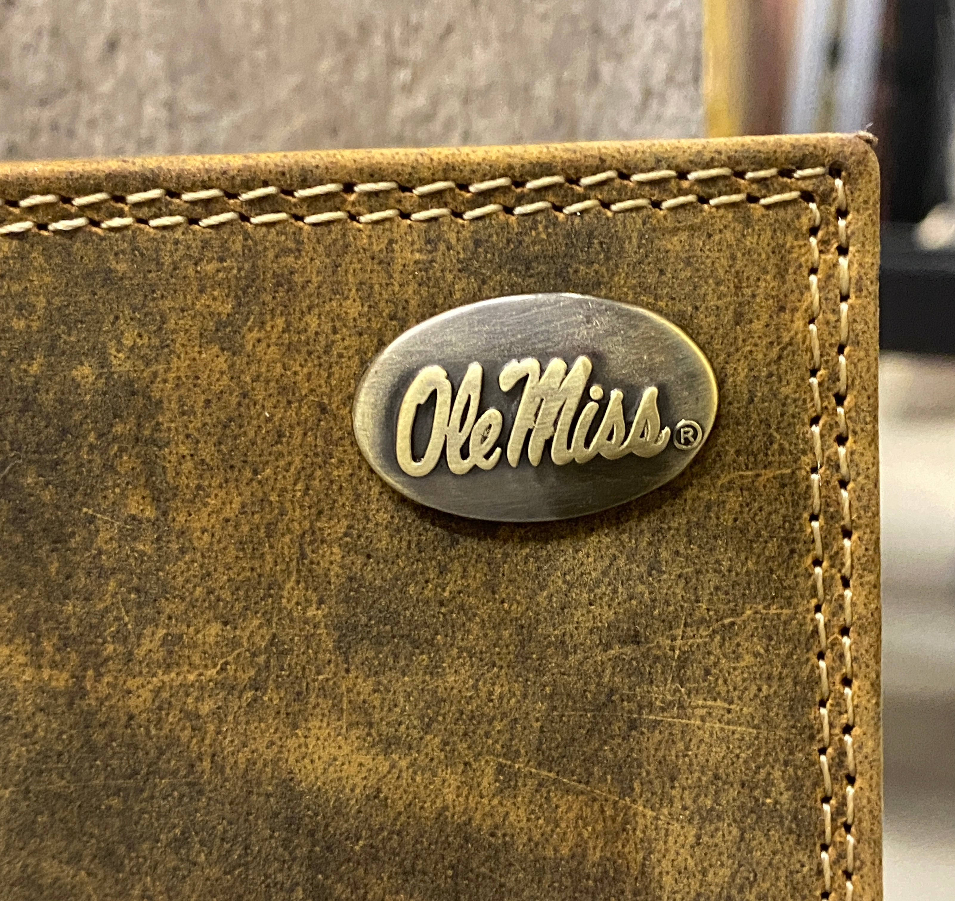 Zep Pro University of Mississippi Vintage Tan Leather Bi-fold Wallet Close up of brass Ole Miss Concho on top right corner.