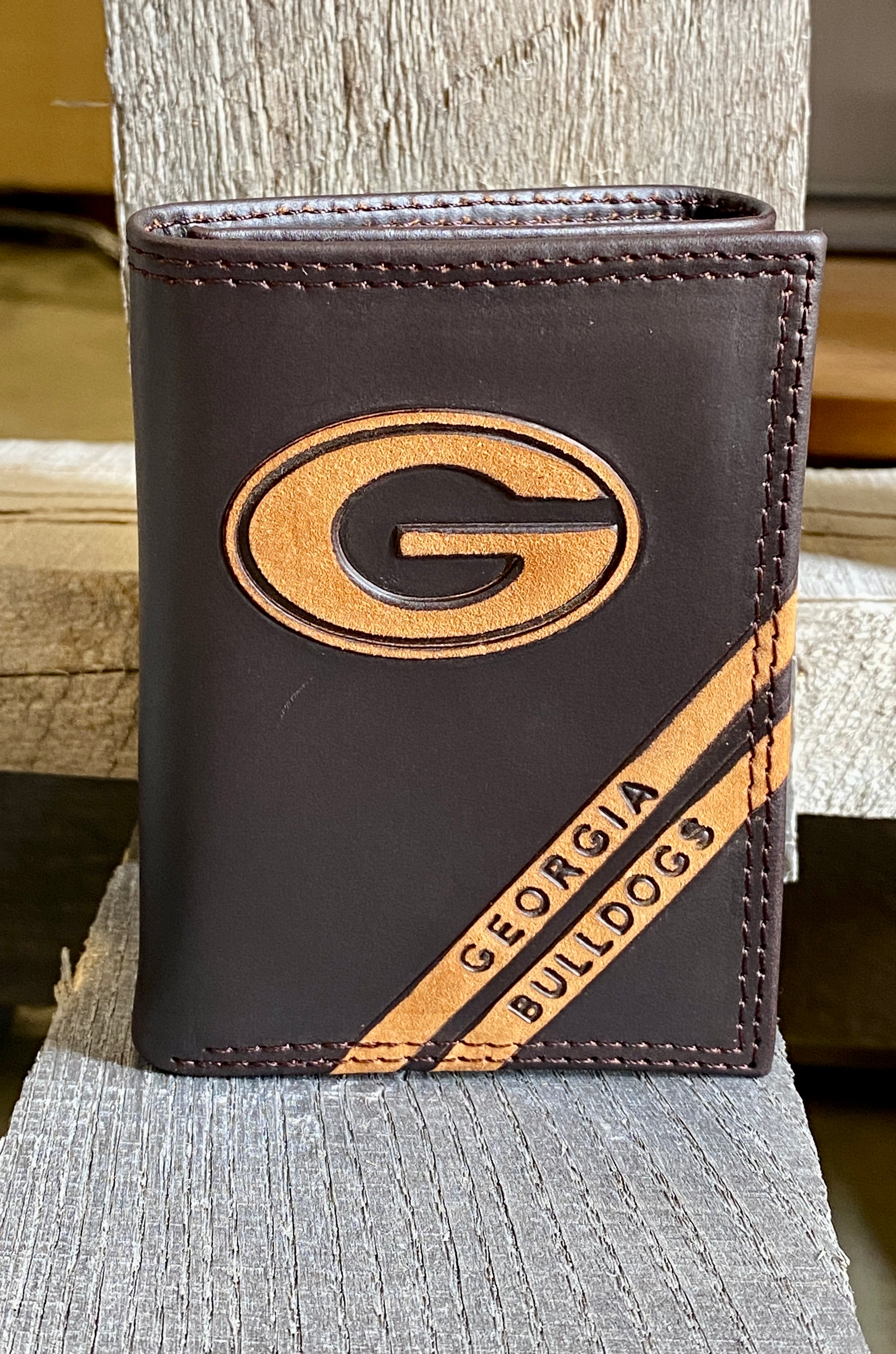 A Zep-Pro brown leather trifold wallet featuring the University of Georgia logo near the wallet top in debossed design. Two debossed stripes angled on the bottom right read Georgia Bulldogs. Front view.